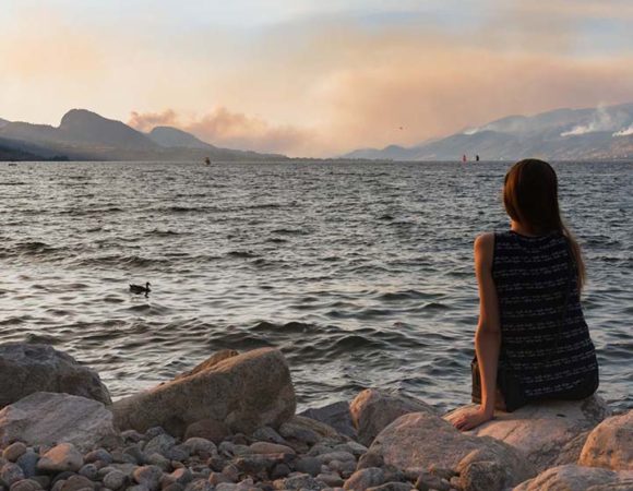 Girl sits by lakeshore at Marine Park in Penticton watching mult M